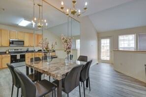 A modern kitchen with a dining area, featuring a large mirror, a chandelier, and a central island with chairs. - Owings Mills Townhouse: 8 Mi to Liberty Reservoir! (Owings Mills)