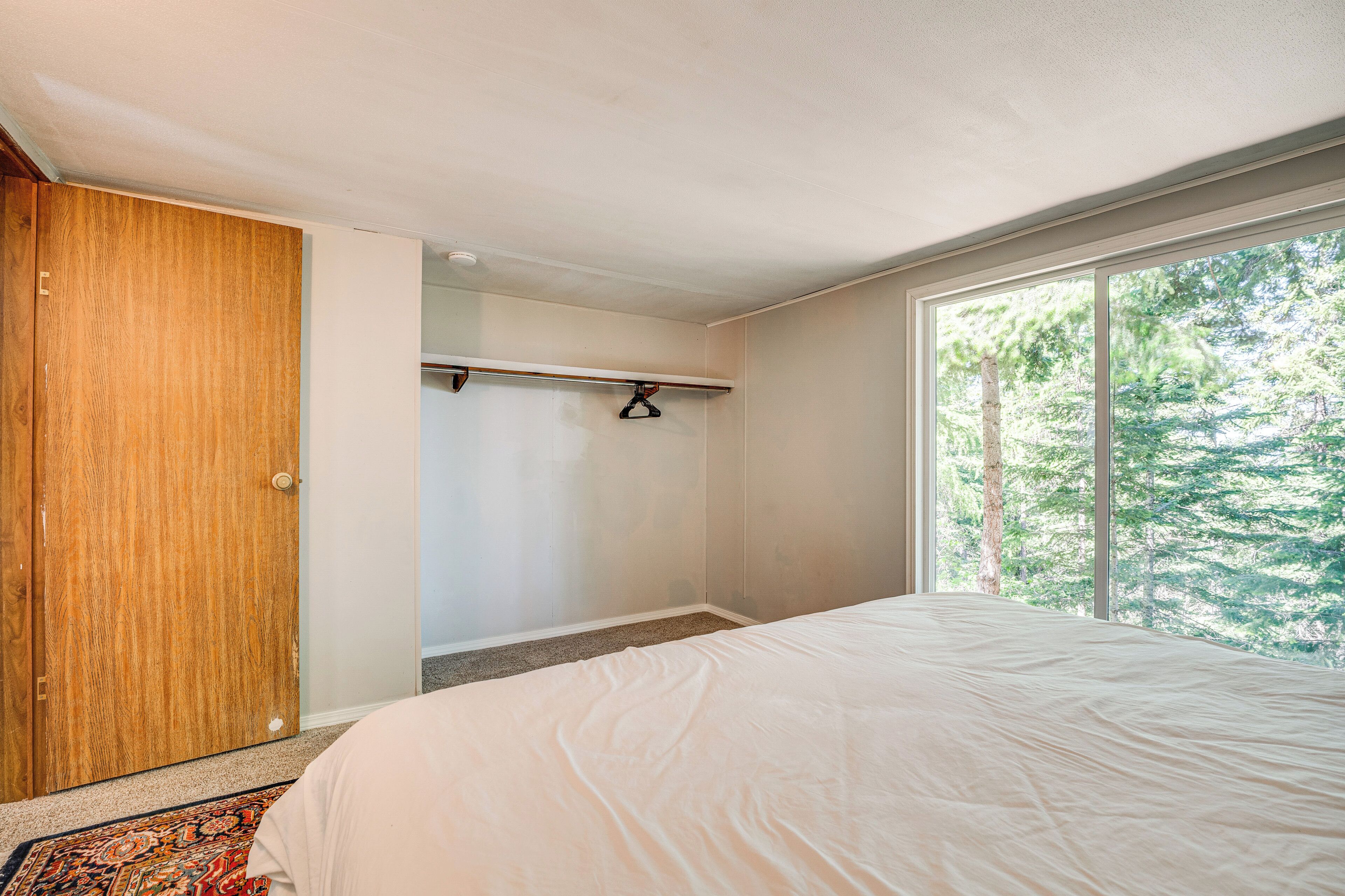 Une chambre avec une grande fenêtre, une porte en bois et un lit recouvert d’une courtepointe blanche.