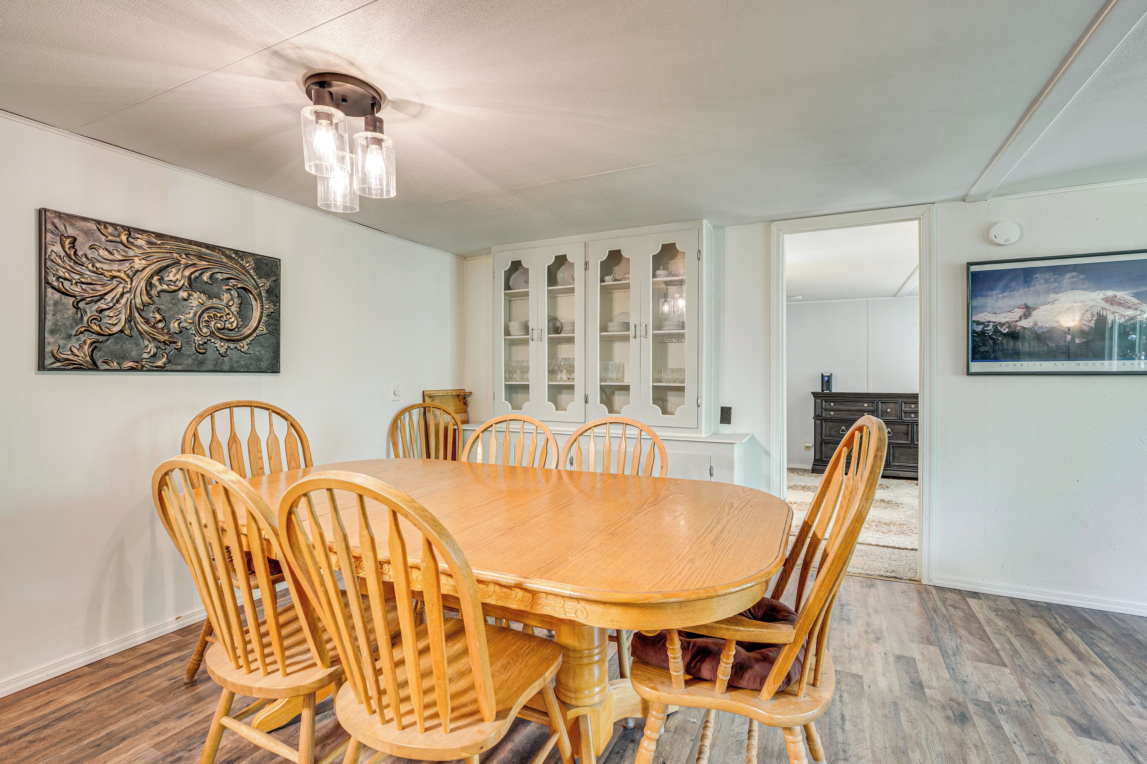 A dining room with a wooden table and chairs, a ceiling light fixture, and a cabinet with glass doors.