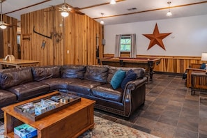 A cozy living room with a leather sofa, wooden walls, a star decoration, and a pool table. - Trails End Lodge: Budget Friendly in Hocking Hills (Logan)