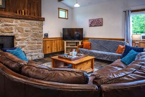 Una sala de estar con chimenea de piedra, sofás de cuero, una mesa de centro de madera y un televisor.