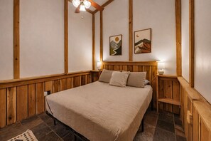A bedroom with a wooden headboard, a bed with a beige quilt, two bedside lamps, and a wooden bench. - Trails End Lodge: Budget Friendly in Hocking Hills (Logan)