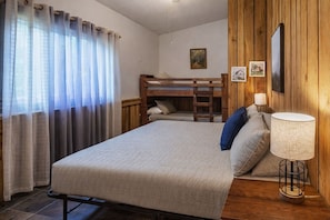 A bedroom with a bunk bed, a bedside lamp, and a window with curtains.
