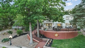 Une maison à deux étages dotée d’une terrasse, d’un espace salon extérieur et d’un chemin en pierre menant à l’entrée.