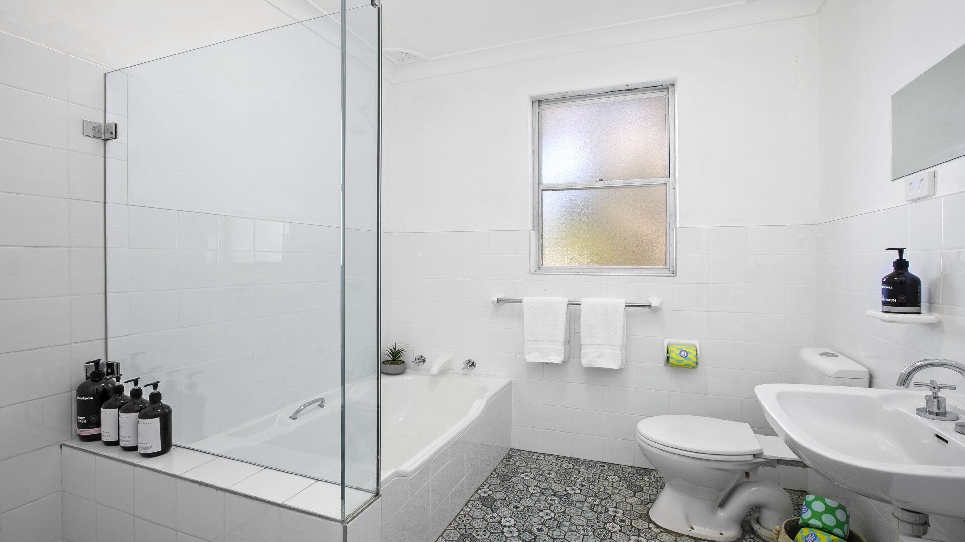 A bathroom with a glass shower enclosure, a bathtub, a toilet, and a sink.