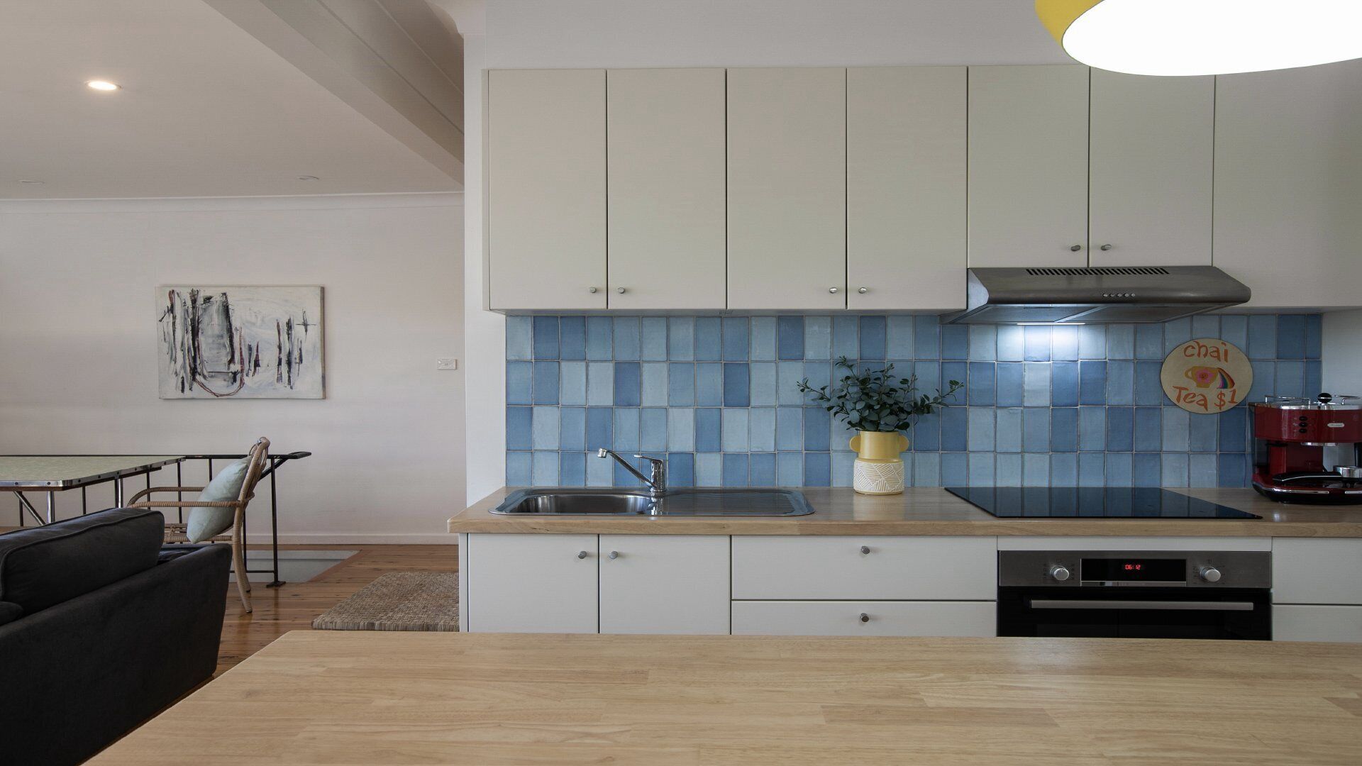 Una cocina moderna con armarios blancos, salpicadero azul, un fregadero, una estufa y una cafetera.