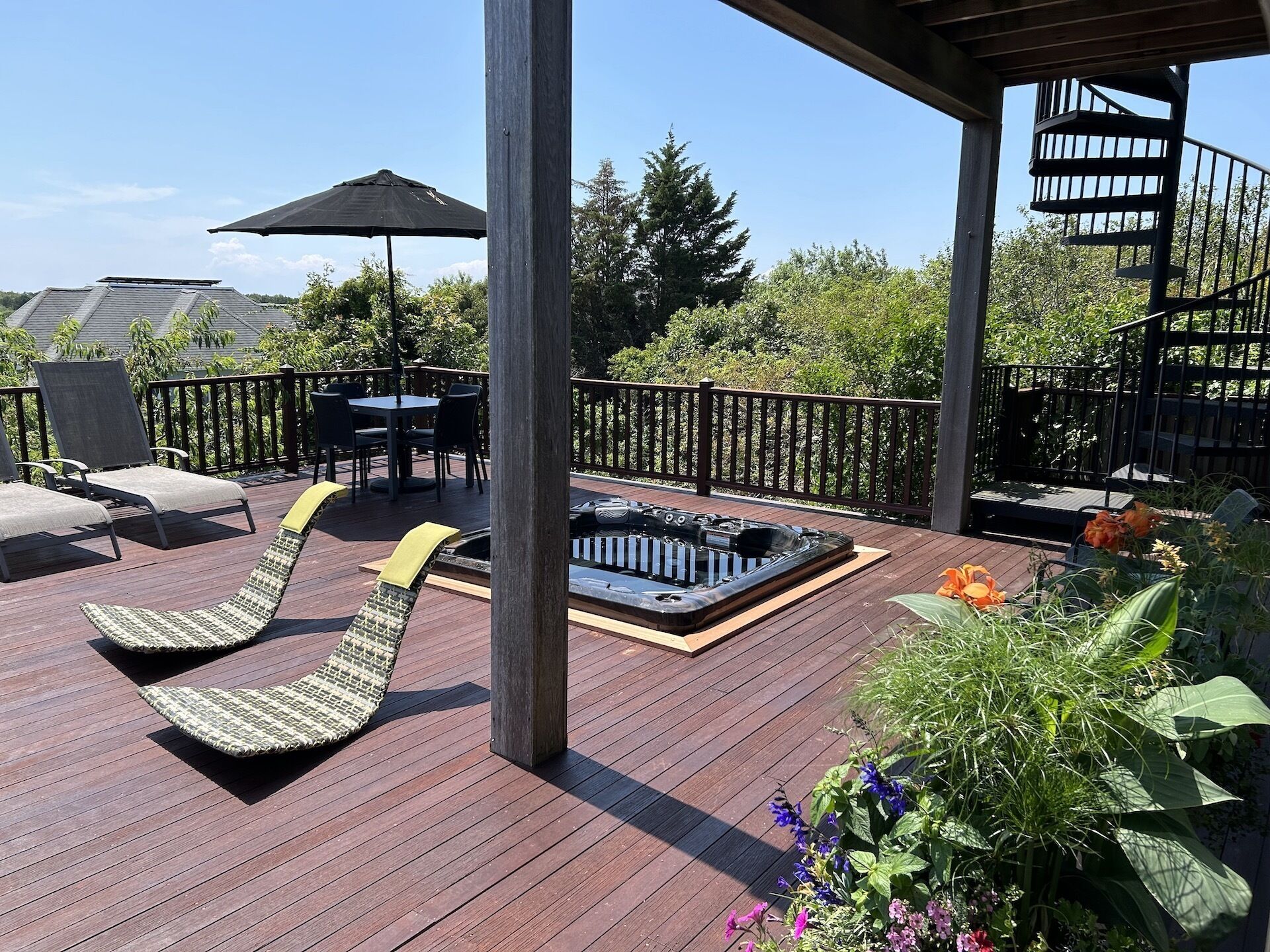 A wooden deck with lounge chairs, a hot tub, and a table with chairs.
