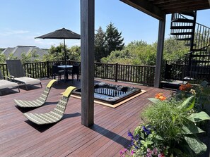 A wooden deck with lounge chairs, a hot tub, and a table with chairs.