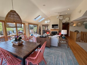 A spacious living area with a wooden dining table, pink chairs, a fireplace, and a television. - Hot Tub & Ocean Views from Deck (Provincetown)