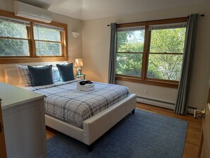 A bedroom with a bed, bedside table, lamp, and large windows with curtains.