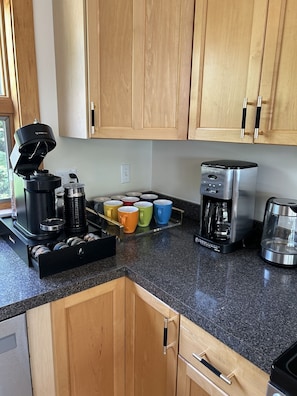 A kitchen with wooden cabinets, a coffee maker, a coffee pot, and a tray with colorful mugs.