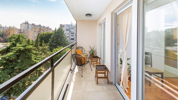 Ein Balkon mit Blick auf eine Stadtlandschaft, ein Stuhl, ein kleiner Tisch und ein Blumentopf.