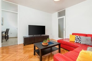 Un salon moderne avec un canapé rouge, un téléviseur à écran plat posé sur un meuble en bois foncé, et une table basse agrémentée de deux plantes en pot.