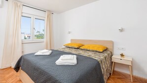 Ein ordentlich bezogenes Bett mit einer grauen Steude, zwei gelben Kissen und gefalteten weißen Handtüchern.