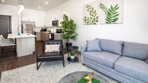 Ein modernes Wohnzimmer mit einem grauen Sofa, einem schwarzen Ledersessel und einem Couchtisch mit Büchern und einem dekorativen Gegenstand.