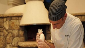 A chef in a white uniform with a striped hat, preparing a pizza on a wooden board in front of a stone oven. - Resort Lubrense - Fiore Di Campo with shared pool (Sant'Agata Sui Due Golfi)