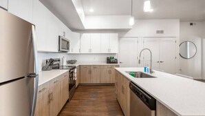A modern kitchen with white cabinets, a stainless steel refrigerator, a dishwasher, and a wooden floor. - Apartment 2108 · Luxury style 2 bed 2 bath apartment (North Salt Lake)