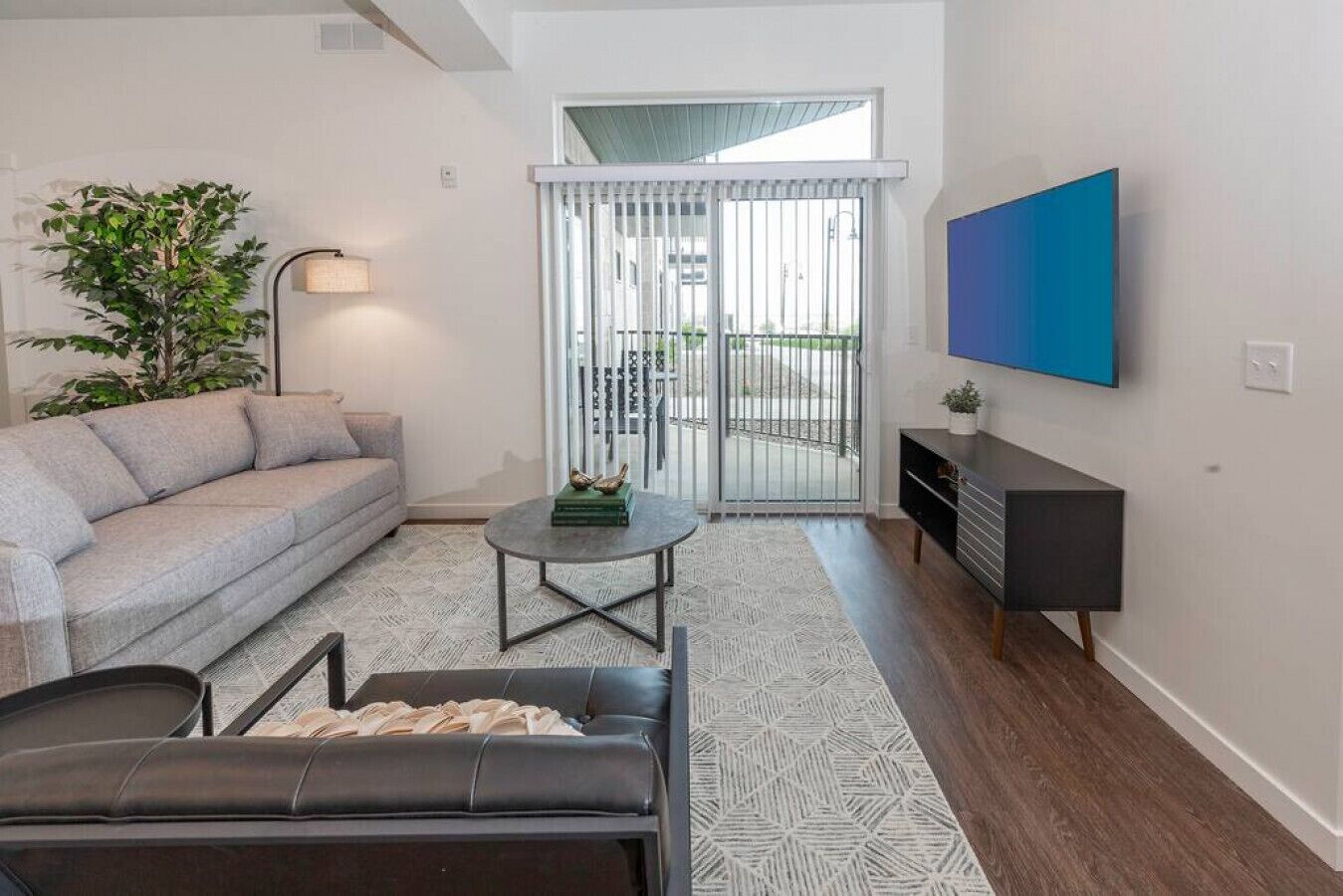 A living room with a sofa, a coffee table, a TV, and a sliding glass door leading to an outdoor area.