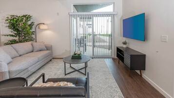 A living room with a sofa, a coffee table, a TV, and a sliding glass door leading to an outdoor area.