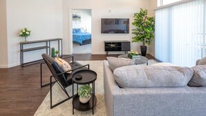 A modern living room with a grey sofa, a black chair, a coffee table, and a TV mounted on the wall. There is a plant and a small table with decorative items. - Apartment 2110 · Luxury style 2 bed 2 bath apartment (North Salt Lake)