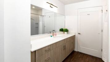 A modern bathroom with a large mirror, a white sink, wooden cabinets, and a door.