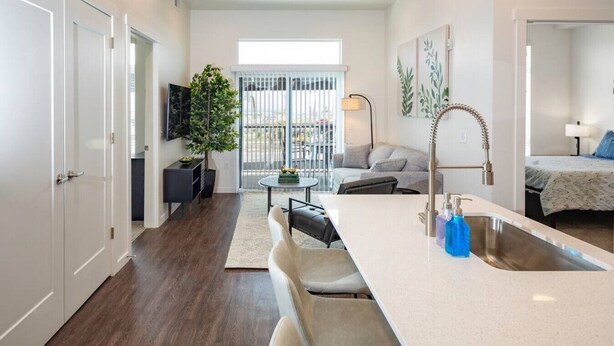 Un appartement moderne comprenant une cuisine, un coin repas et un salon. Il est doté d’une grande fenêtre, d’une plante en pot et d’un téléviseur à écran plat.