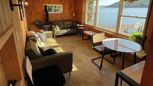 Une pièce chaleureuse au décor intérieur en bois, avec un canapé vert, une petite table et une vue sur un lac, visible à travers de grandes fenêtres.