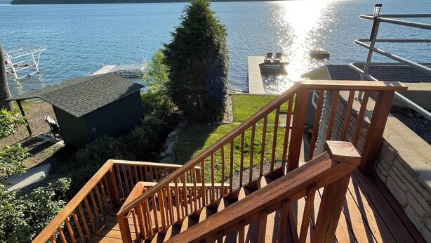 Une terrasse en bois avec une rambarde, un petit abri de jardin et une vue sur un lac où l’on peut voir des bateaux.