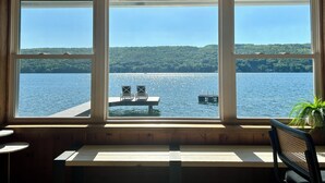 Une pièce dotée d’une grande fenêtre donnant sur un lac, de murs en bois et d’un banc avec deux chaises.
