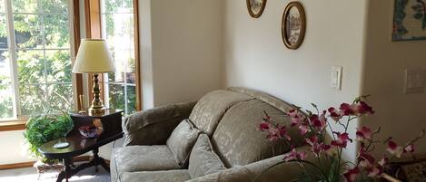 Una sala de estar acogedora con un sofá color beige, una mesa con lámpara y una ventana con vistas a zonas verdes.