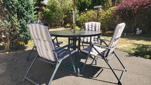 A round metal table with four striped chairs, set on a gravel patio surrounded by greenery and a wooden fence. - Gresham House: Your home away from home... A comfy, cozy corner of Gresham.  (Gresham)