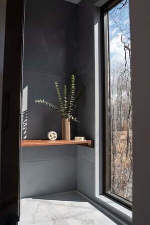 A corner room with a dark wall, a window, a wooden shelf, and a potted plant. - Refuge Bay's Aqua Tiny Home - Luxury Off Grid Escape (Cherhill)
