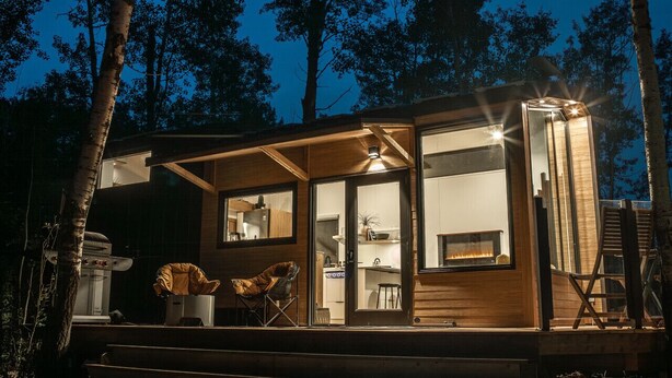 A cabin with a large glass door, a fireplace, and a deck area.