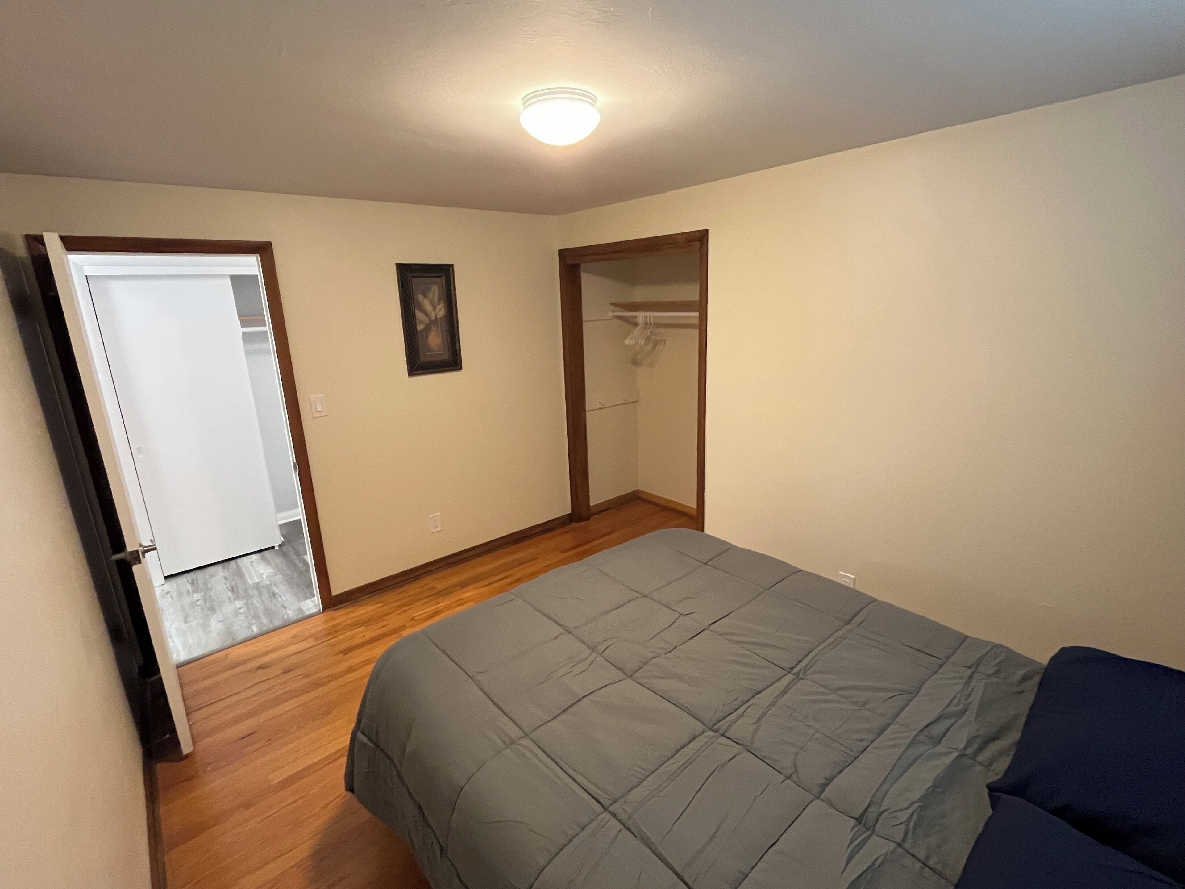Een slaapkamer met een bed, houten vloeren, een kast en een deur naar een andere kamer.