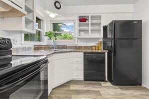 Une cuisine moderne avec des meubles blancs, un réfrigérateur noir, un lave-vaisselle et une fenêtre donnant sur un espace verdoyant.