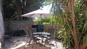 Un patio al aire libre con muro de piedra, una mesa con sillas, un banco y un gran paraguas que da sombra.