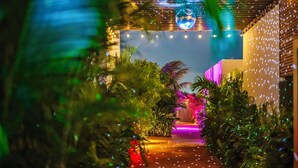 A pathway with plants and string lights leading to a brightly lit area. - Privada Stays - Private Pools & Colorful-Chic Boutique Hotel - Adults Only (Oranjestad)