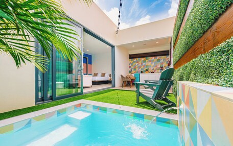 A modern pool area with a glass-enclosed room, a green lawn, and a colorful geometric wall.