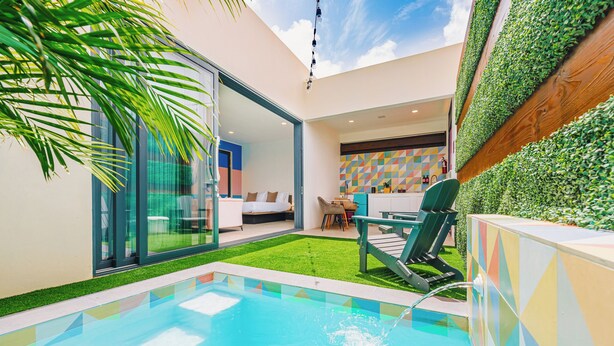 A modern pool area with a glass-enclosed room, a green lawn, and a colorful geometric wall. - Privada Stays - Private Pools & Colorful-Chic Boutique Hotel - Adults Only (Oranjestad)
