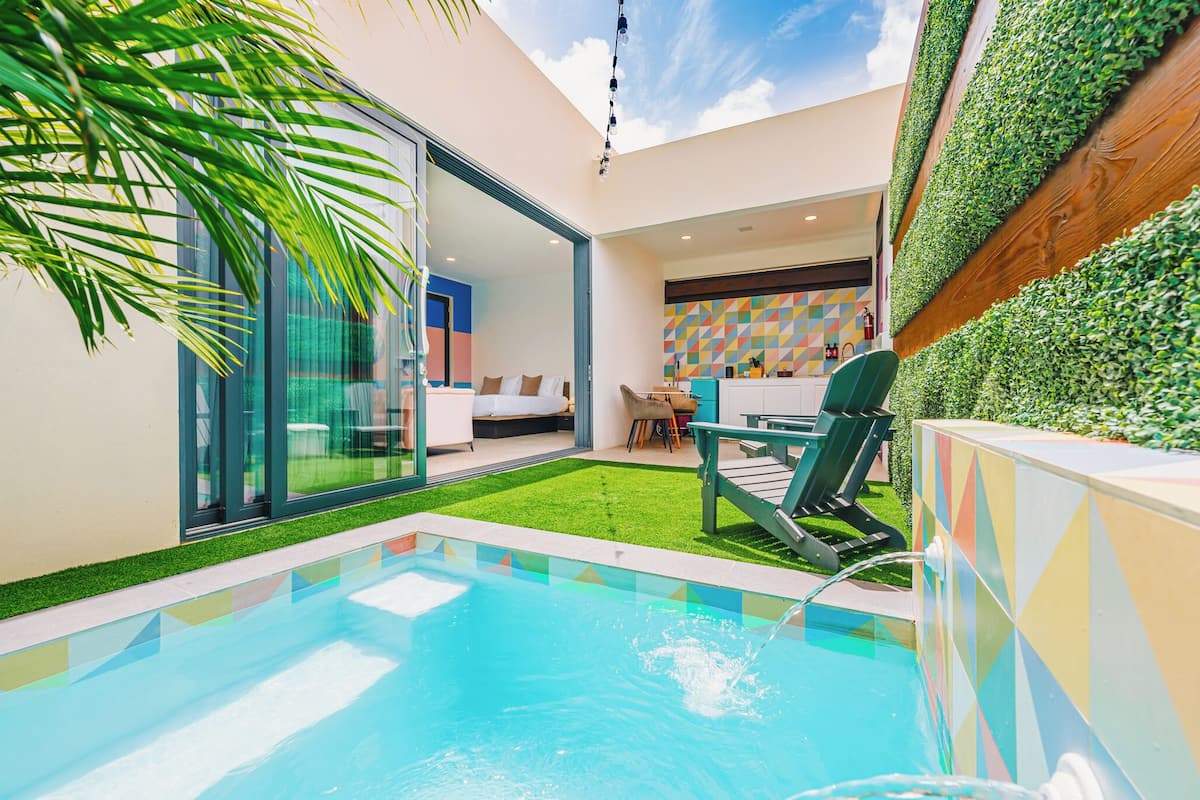Un espace piscine moderne doté d’une pièce fermée par des parois de verre, d’une pelouse verdoyante et d’un mur géométrique aux couleurs vives.