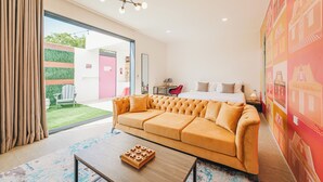 A modern hotel room with a large bed, a sofa, a coffee table, and a view of the garden. - Privada Stays - Private Pools & Colorful-Chic Boutique Hotel - Adults Only (Oranjestad)