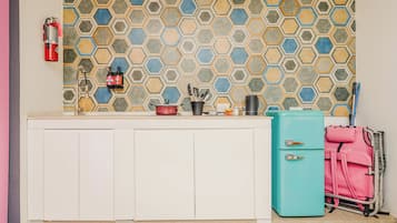 Una cocina con salpicadero de azulejos hexagonales, encimera blanca, maleta rosa y refrigerador verde azulado.