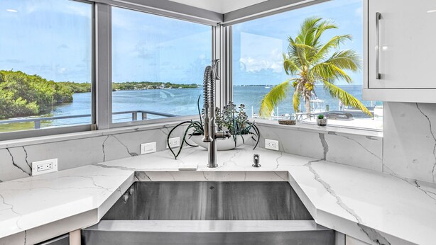 A kitchen with a large window overlooking a body of water, a sink, and a plant on the counter. - Key Largo Home 3 Bed/3 Bath (Key Largo)