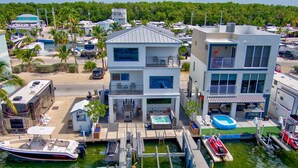 A multi-story building with a pool, outdoor seating, and a dock with boats. - Key Largo Home 3 Bed/3 Bath (Key Largo)