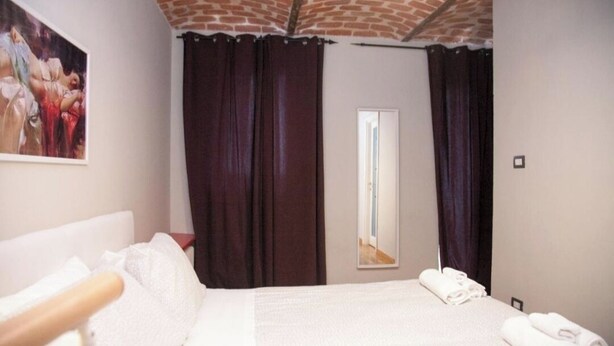 Ein Hotelzimmer mit einem Bett, einem Spiegel, dunklen Vorhängen und einem Bild an der Wand.