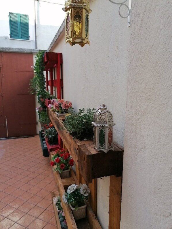 Un étroit couloir extérieur avec un banc en bois, des plantes en pot et des lanternes suspendues.