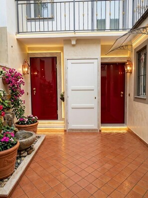 A building entrance with a red door, a white door, and a balcony with a railing.
