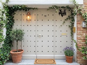Une porte blanche portant le numéro « 11 » et l’inscription « COURRIER », entourée de verdure et agrémentée d’une plante en pot.