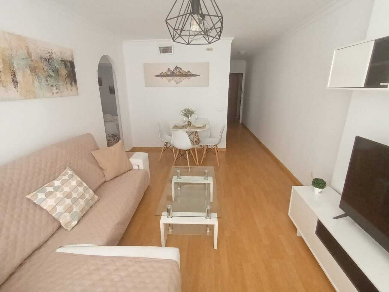 Een moderne woonkamer met een bank, salontafel, televisie en een eethoek met stoelen en een kleine tafel.