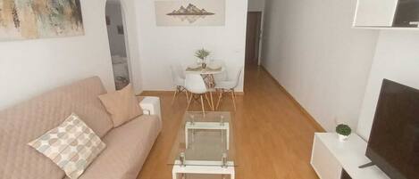 Een moderne woonkamer met een bank, salontafel, televisie en een eethoek met stoelen en een kleine tafel.